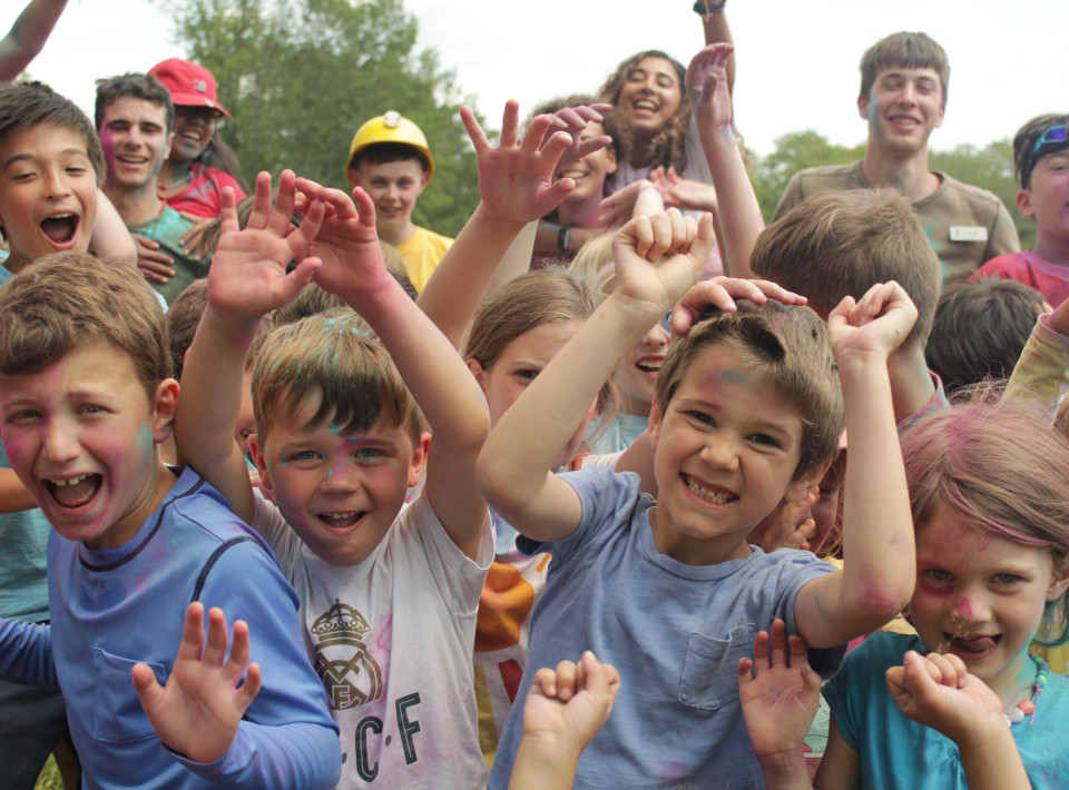 Joyful day campers throwing their hands up during a color-powder celebration