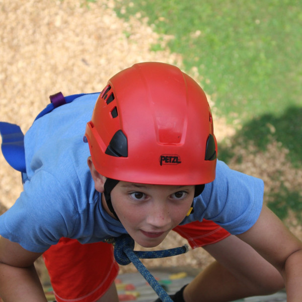 Young camper in a red Petzl helmet climbing on the high ropes course