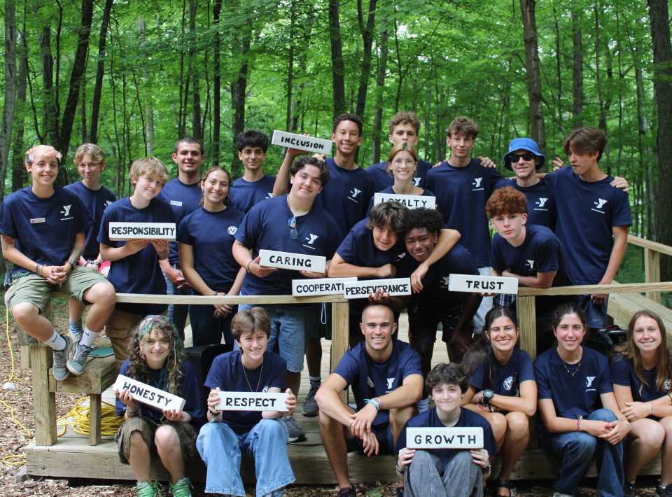 Camp Sloane teen leadership group in the forest holding hand-painted signs reading Caring, Honesty, Respect, Responsibility, Inclusion, Loyalty, Cooperation, Perseverance, Trust and Growth
