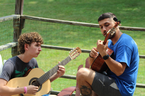Two campers playing acoustic guitars together on a wooden porch